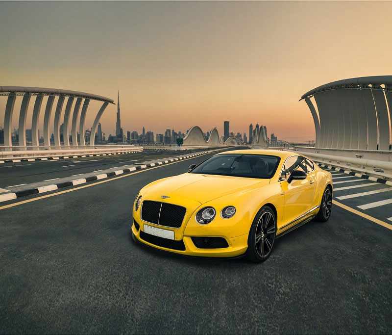Yellow Bentley Continental GT on a bridge with the Dubai skyline behind it