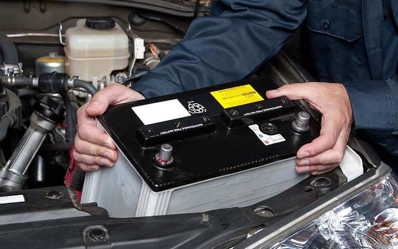 A replacement 12-volt battery being positioned in an engine bay