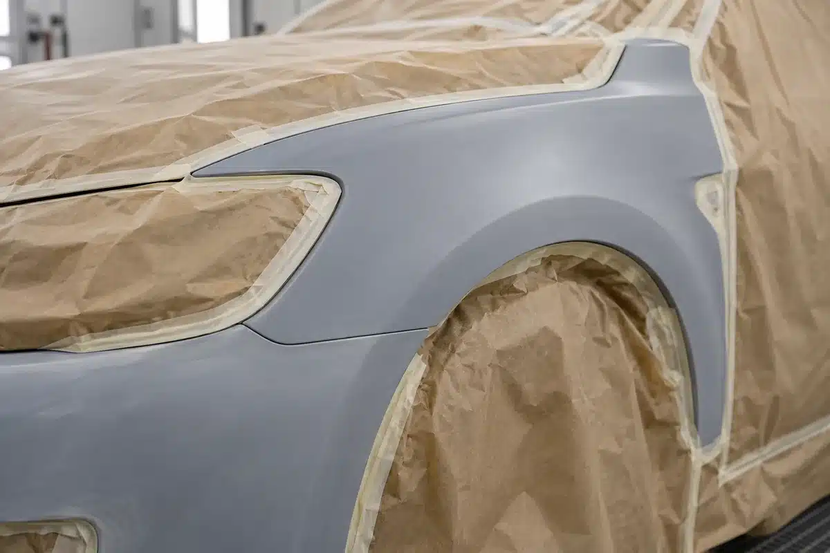 Primed car fender with neighboring areas masked before repainting