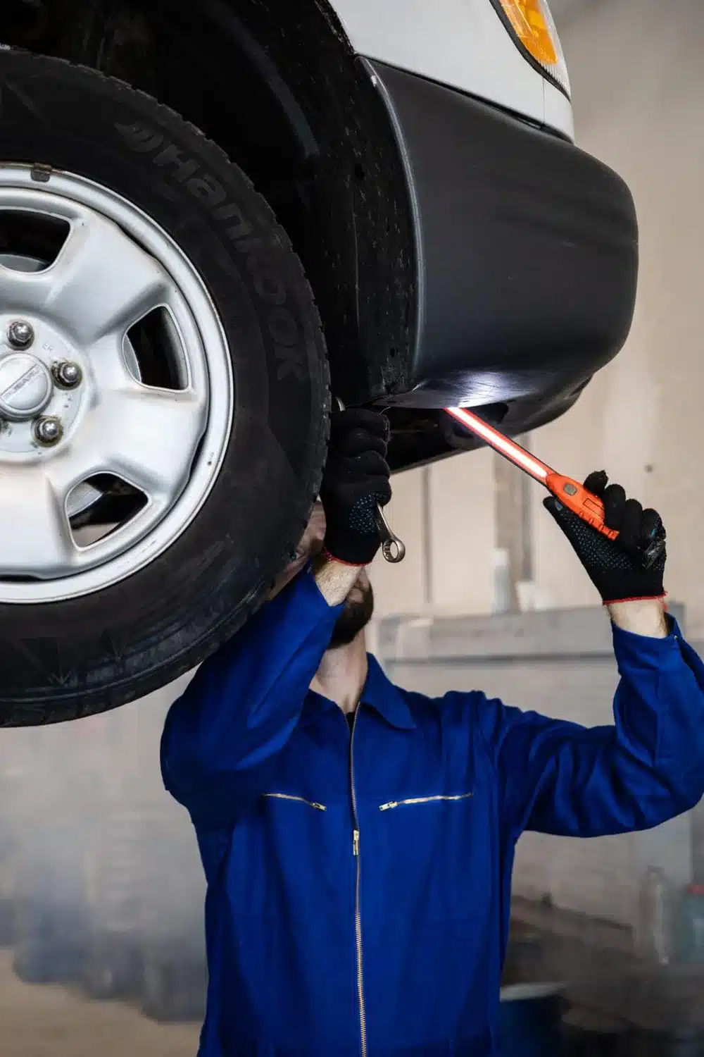 Technician using a work light to inspect the underside of a raised vehicle