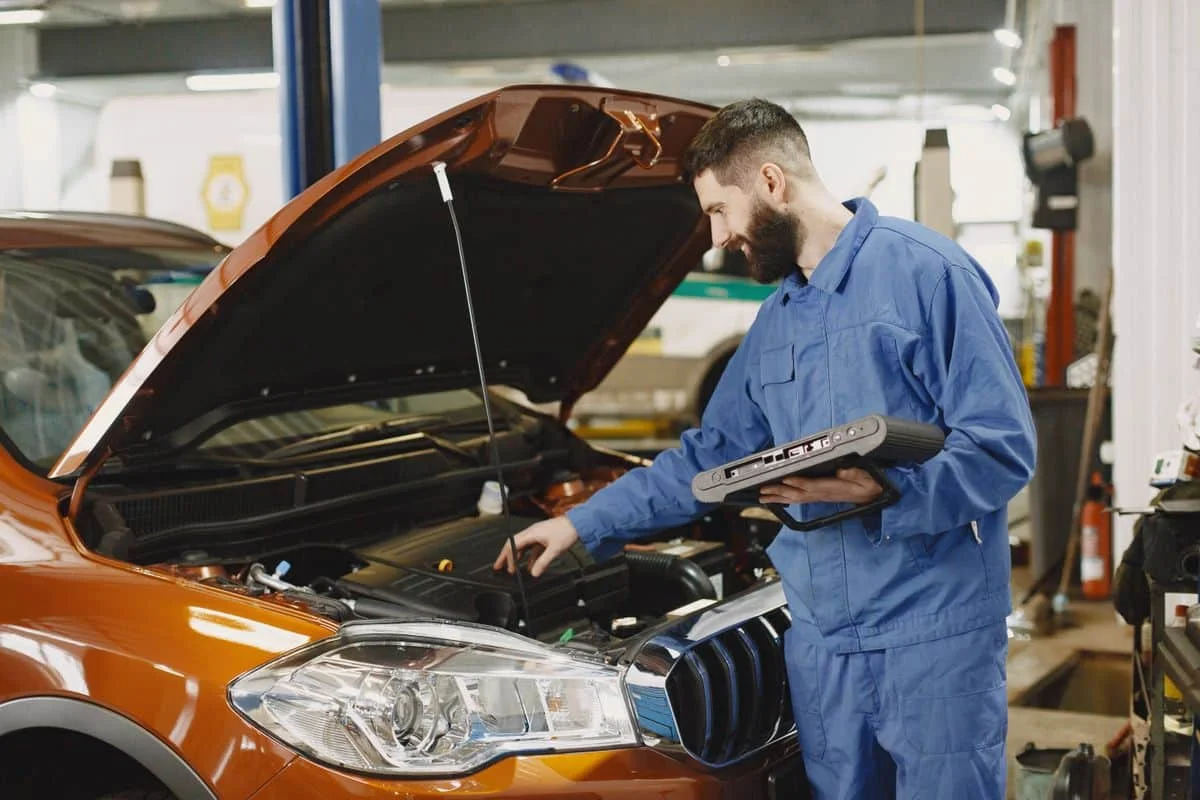 Technician checking a vehicle engine bay with diagnostic equipment