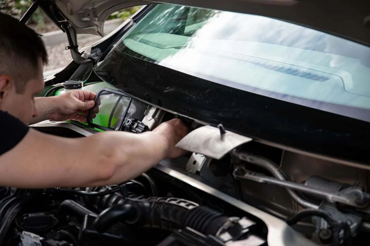 Hands working on mechanical components in a car engine bay