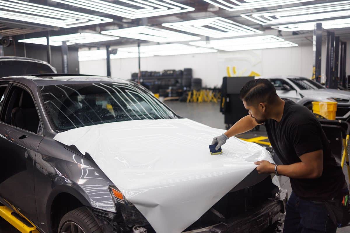 Installer using a squeegee to apply white vinyl film across a car hood