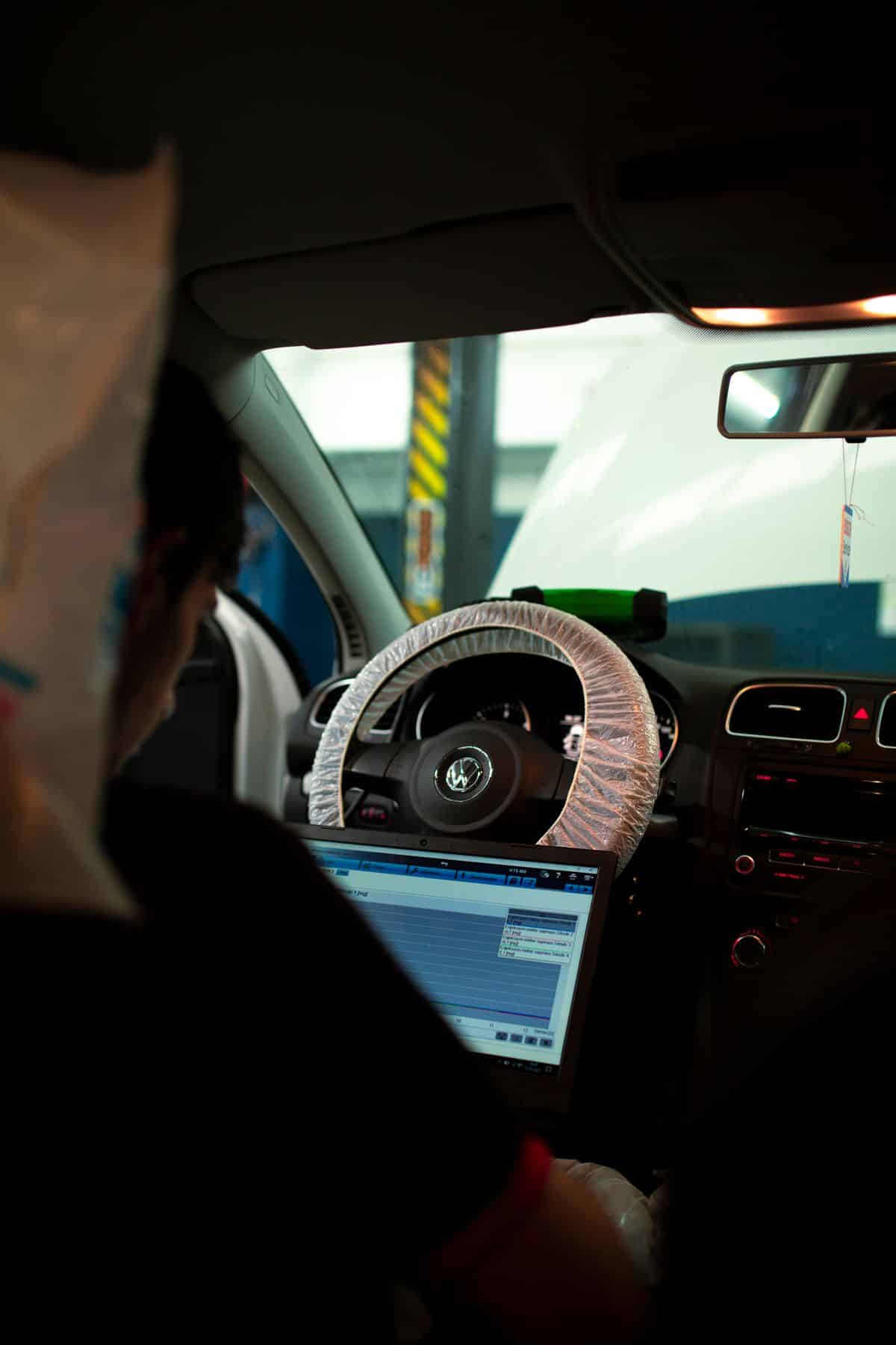 Technician reviewing a diagnostic laptop from the driver's seat of a car