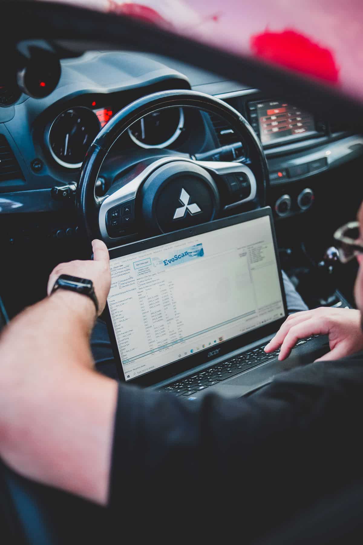 Technician using a diagnostic laptop inside a parked car