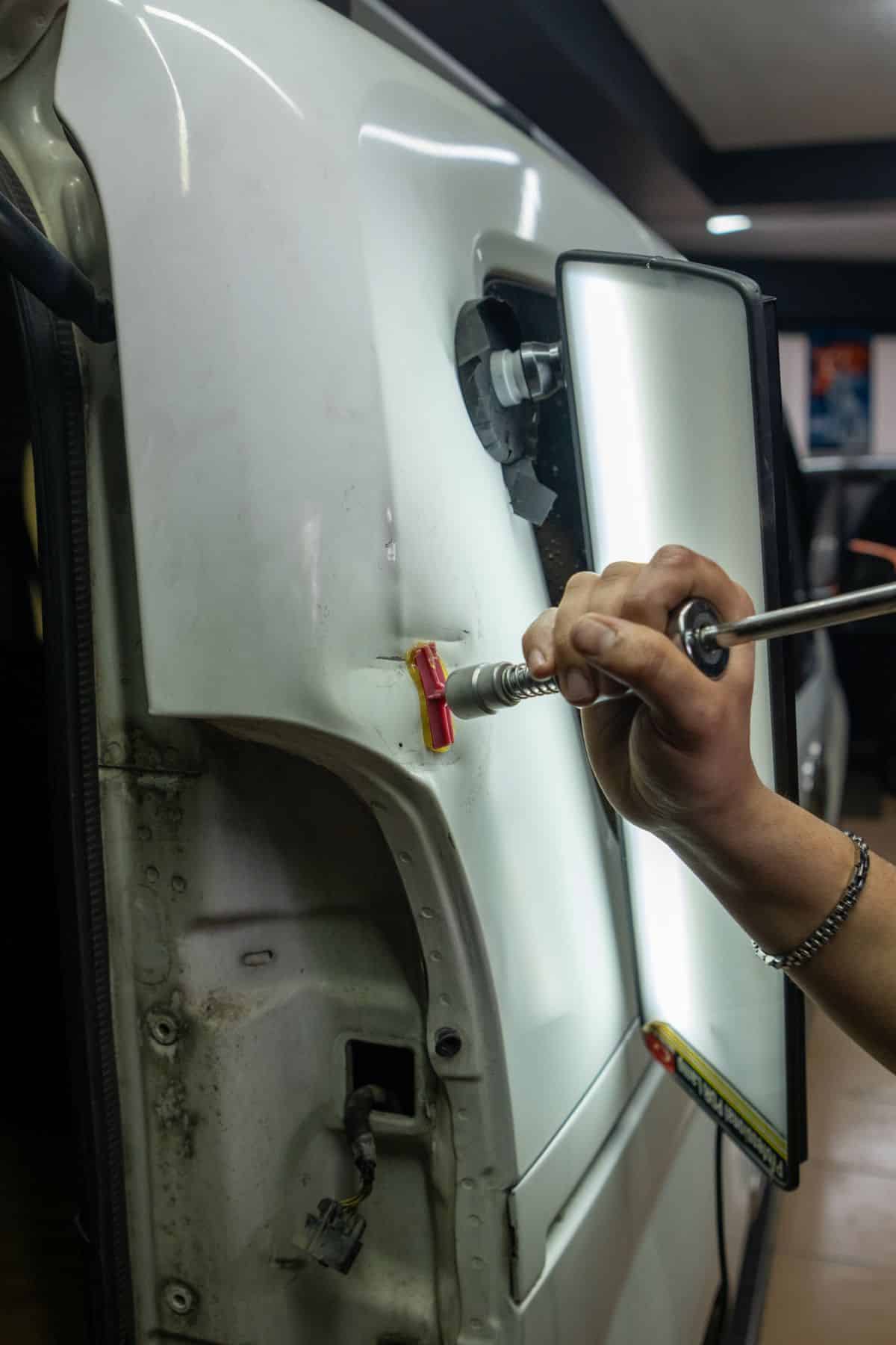 Technician using a glue pulling tool and inspection light on a damaged car panel