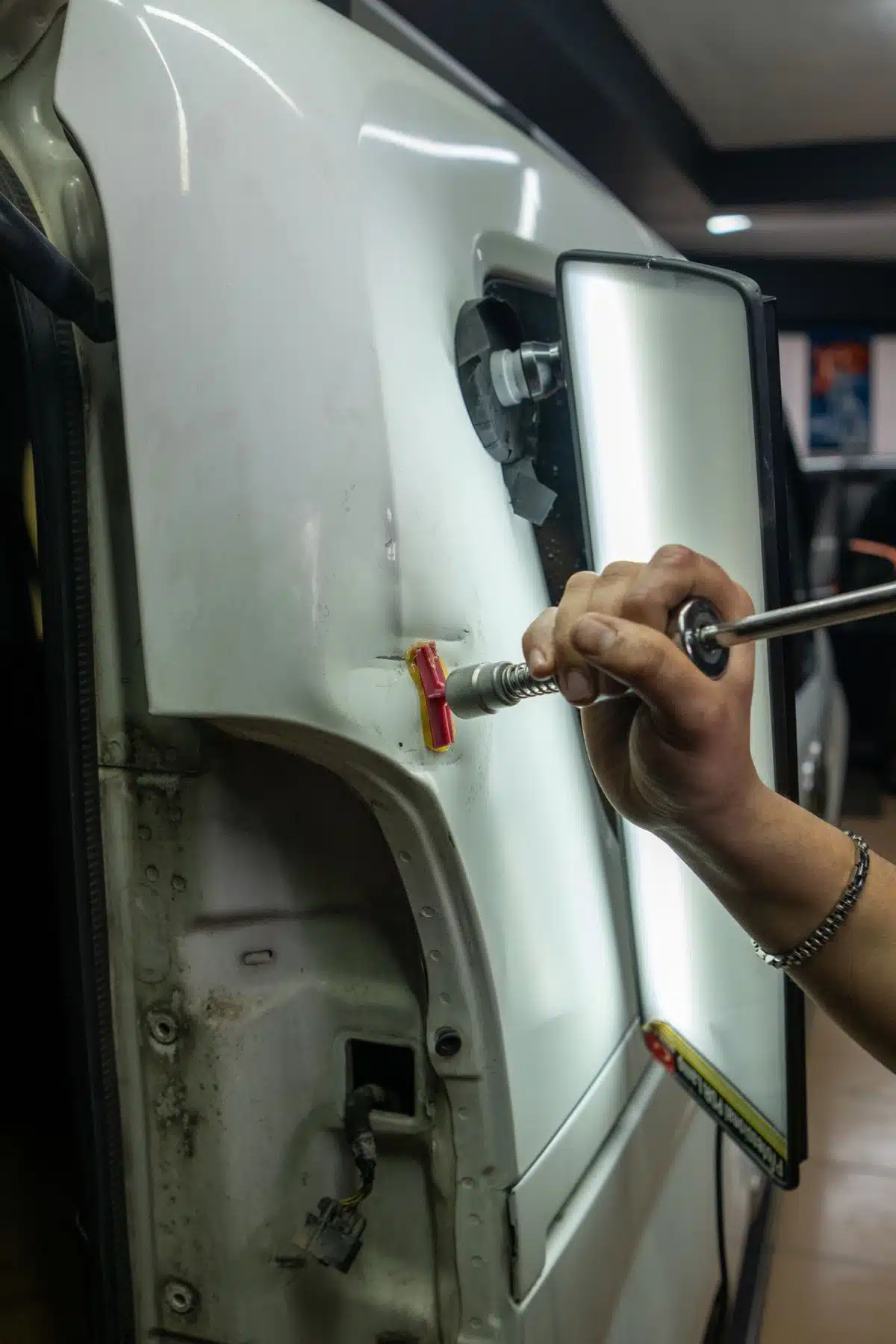 Technician using a glue-pulling tool beside a reflection light on a car panel