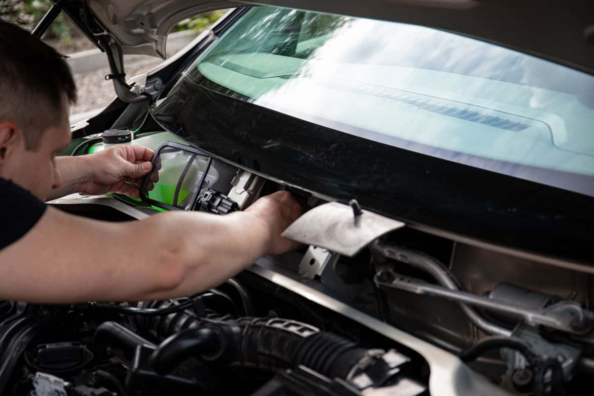 Mechanic accessing a filter near the windshield during vehicle servicing