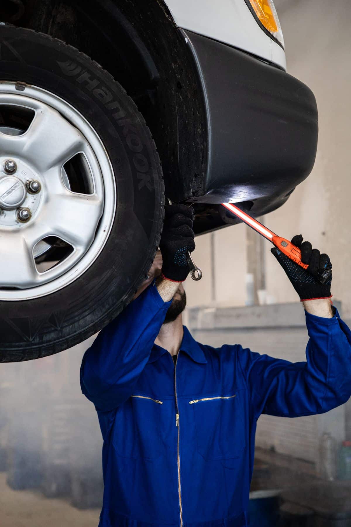 Mechanic inspecting the underside of a raised car with a work light