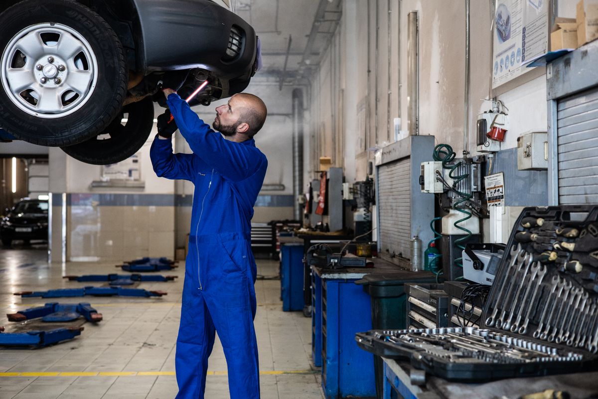 Technician inspecting a vehicle wheel and underbody in a service workshop