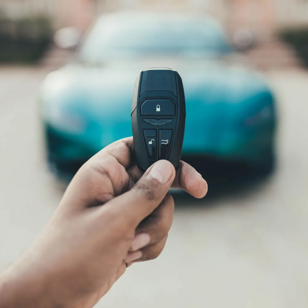 A hand holding an Aston Martin key with a green car in the background