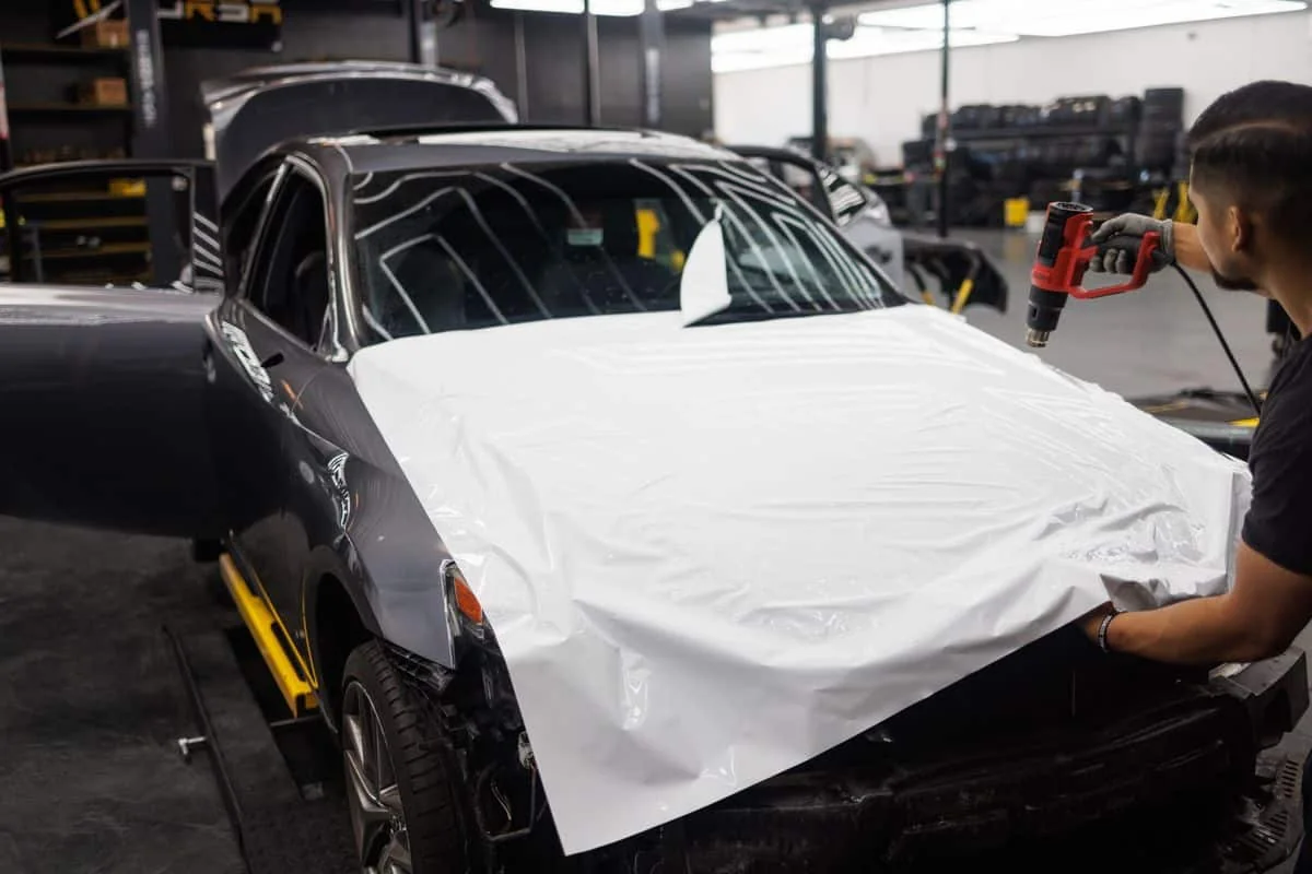 Technicians positioning white vinyl film across a car bonnet