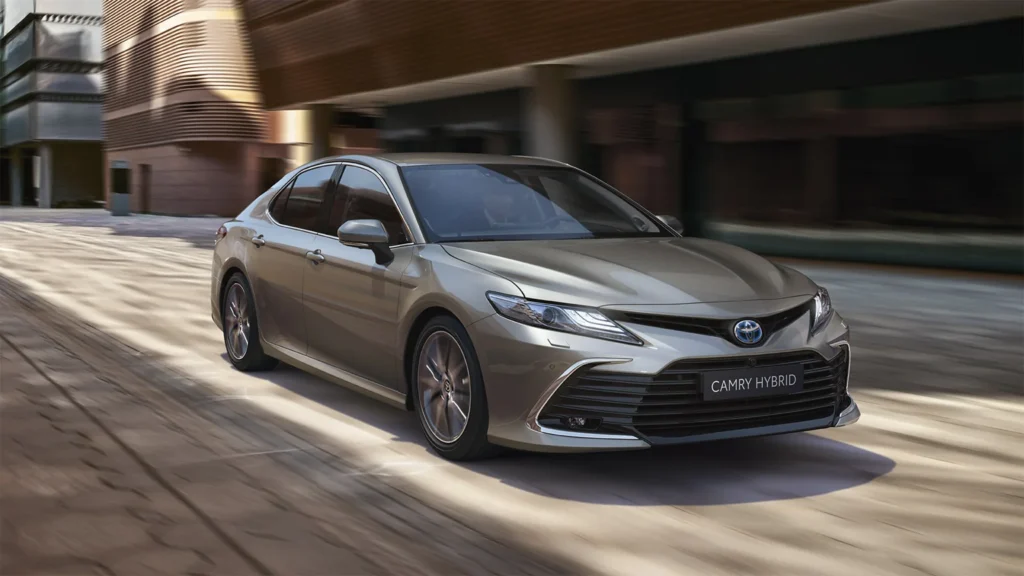 Earlier-generation Toyota Camry Hybrid driving past buildings