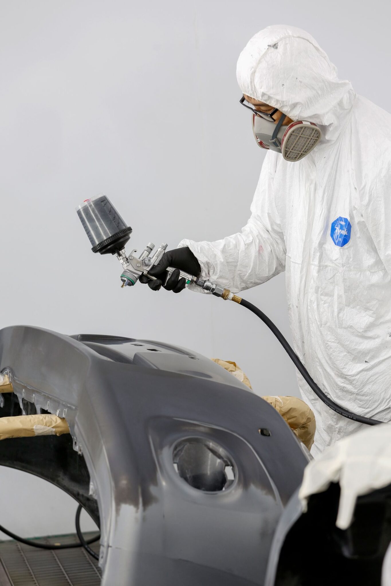 Technician in protective clothing spray painting a removed bumper