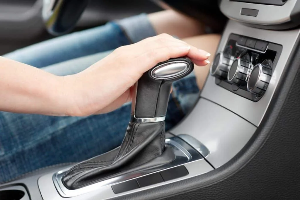Hand resting on a manual gear selector inside a car