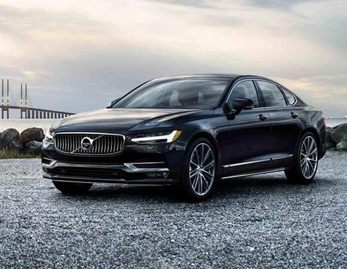 Black Volvo S90 saloon beside a rocky waterfront